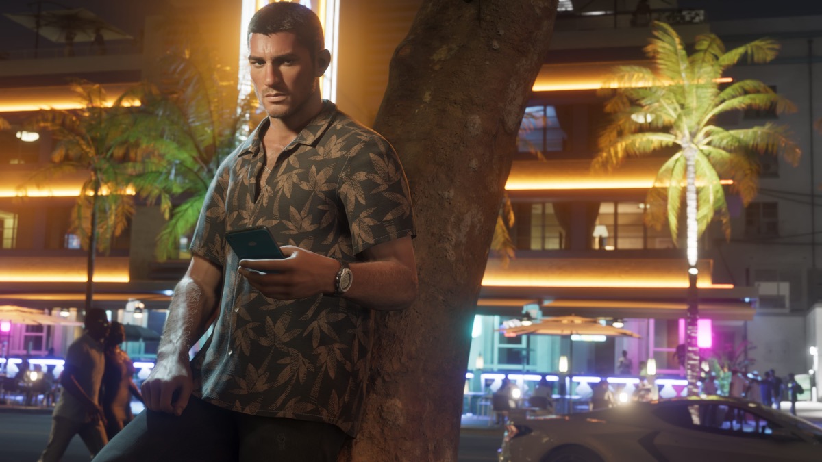Capture officielle GTA 6 : Jason Duval adossé à un arbre dans une rue de Vice City au crépuscule, téléphone en main, néons en arrière-plan.